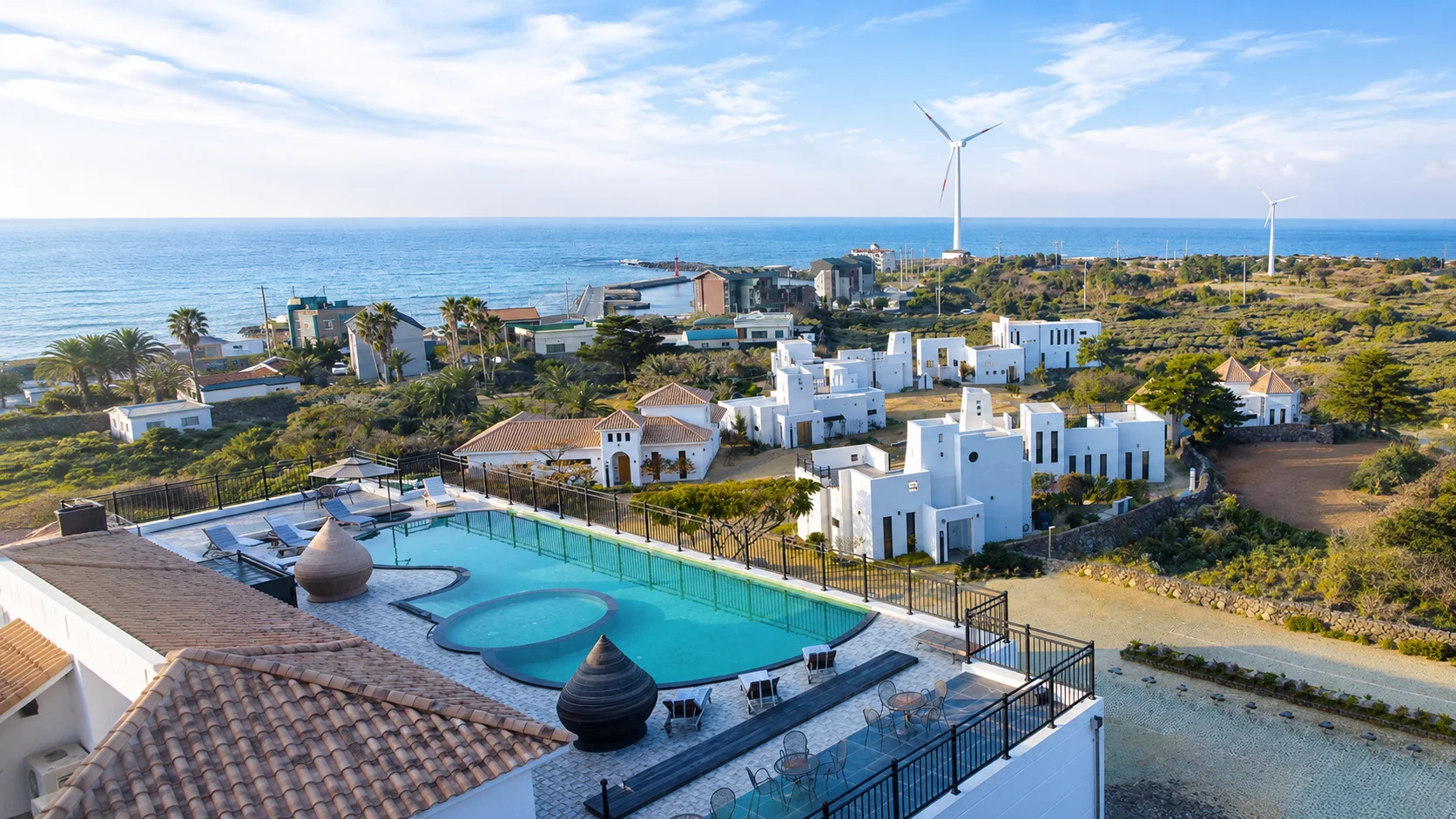 View of RITAMVILLE Jeju Village with the sea, a wind turbine, white buildings, and a pool